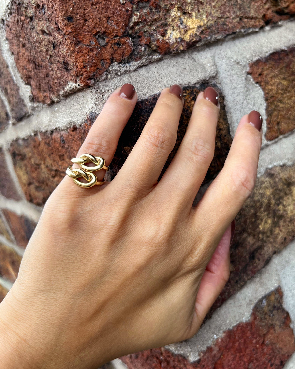 Two vintage Irish 9kt gold knot rings stacked together on a pinky finger against a red brick wall.