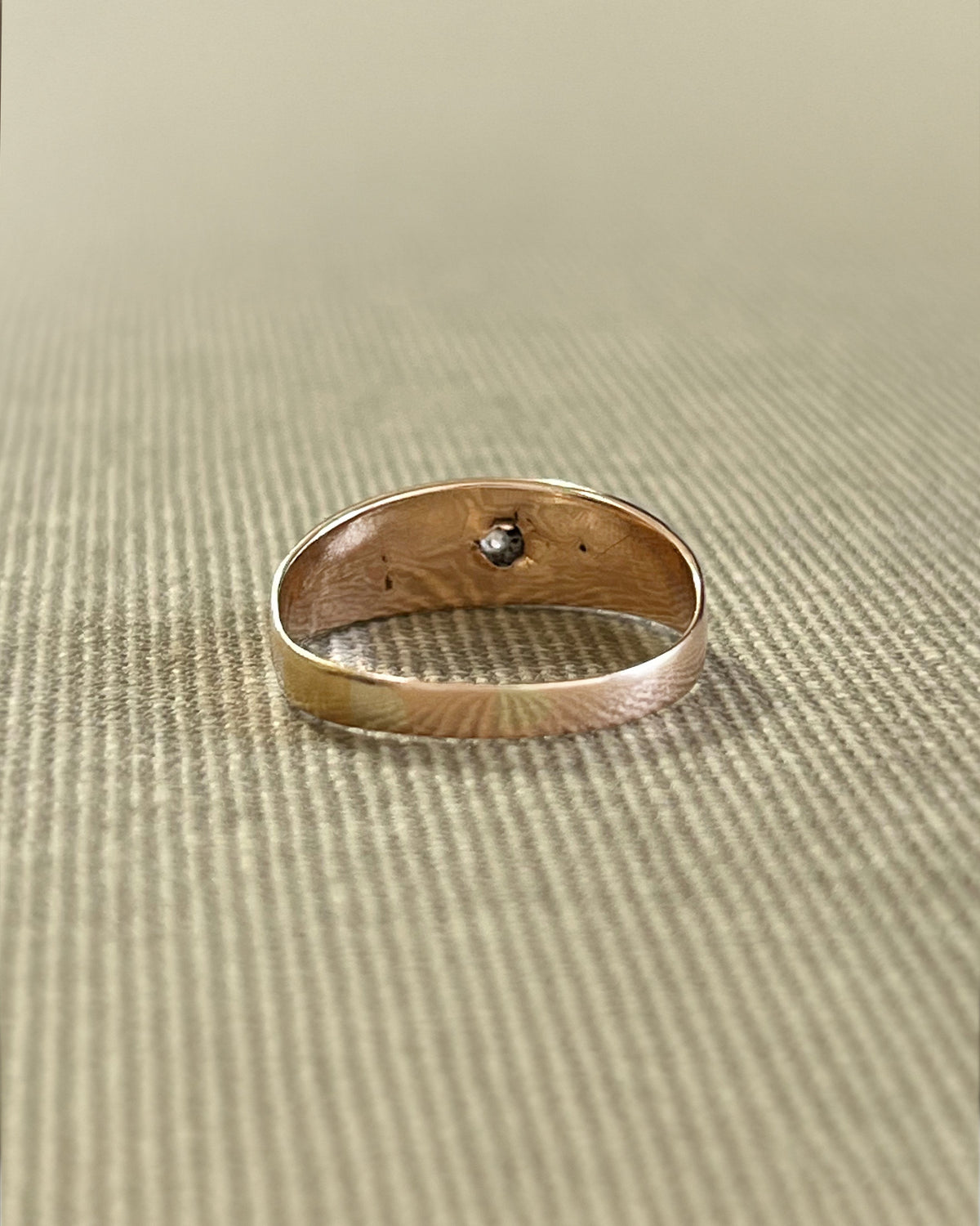 Reverse view of an antique 15kt gold gypsy set ring showing the engraved shoulders and smooth gold shank against a beige canvas background.