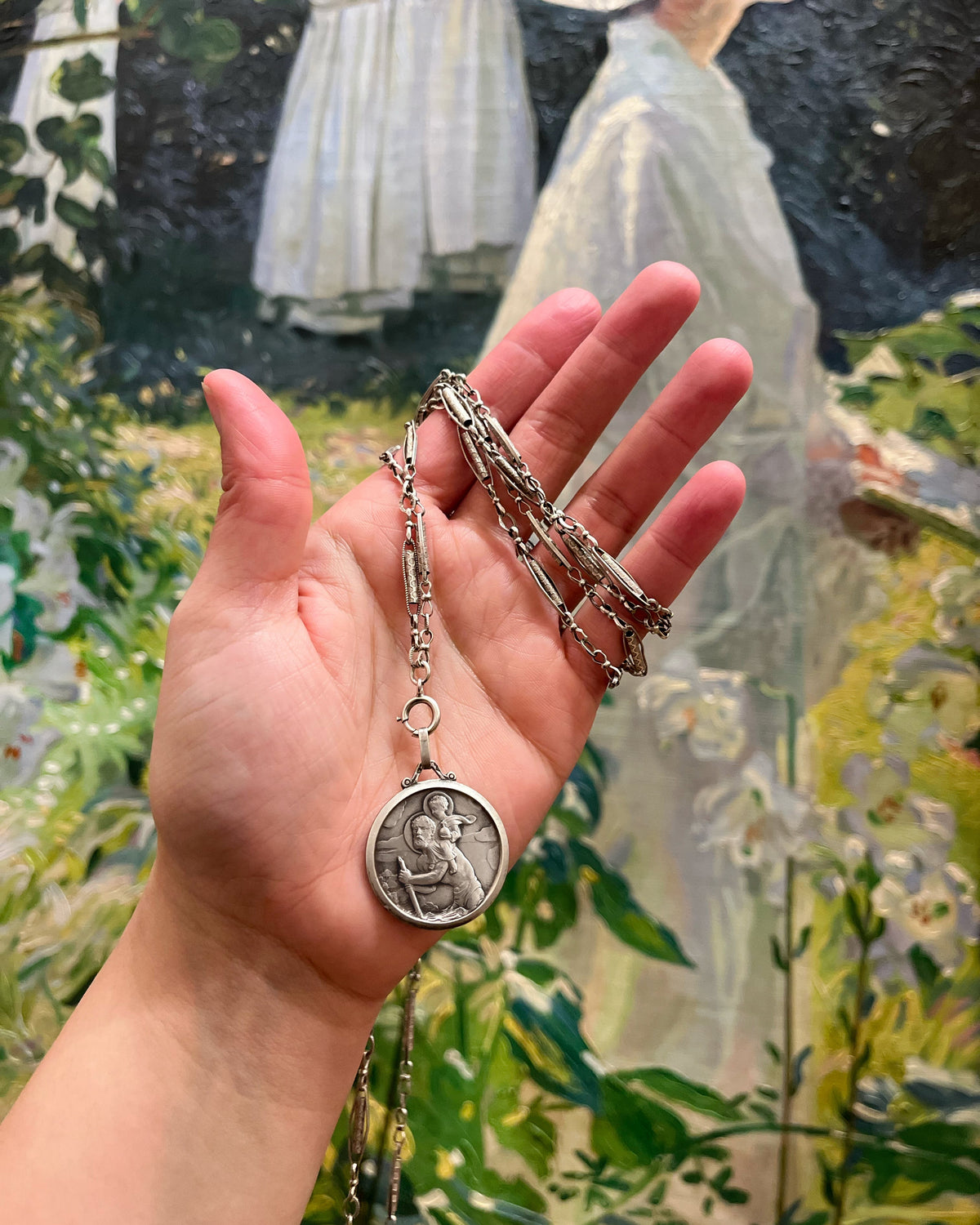 Belle Époque French antique silver sautoir necklace wrapped around a hand and suspending a St. Christopher pendant, styled against a painted background.