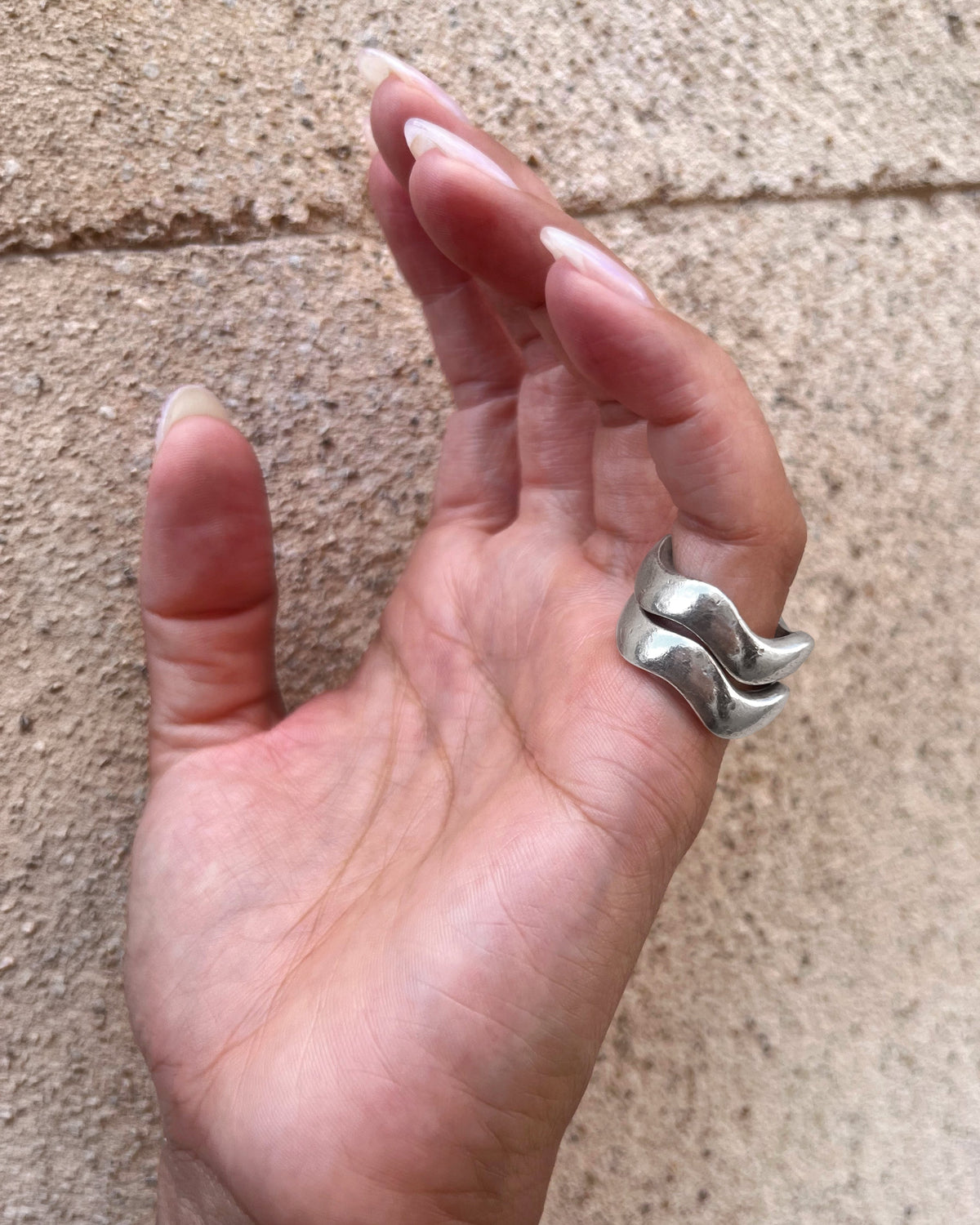 Set of two modernist vintage sterling silver wave rings shown stacked on a pinky finger, demonstrating their gently curving flush-fitting design.