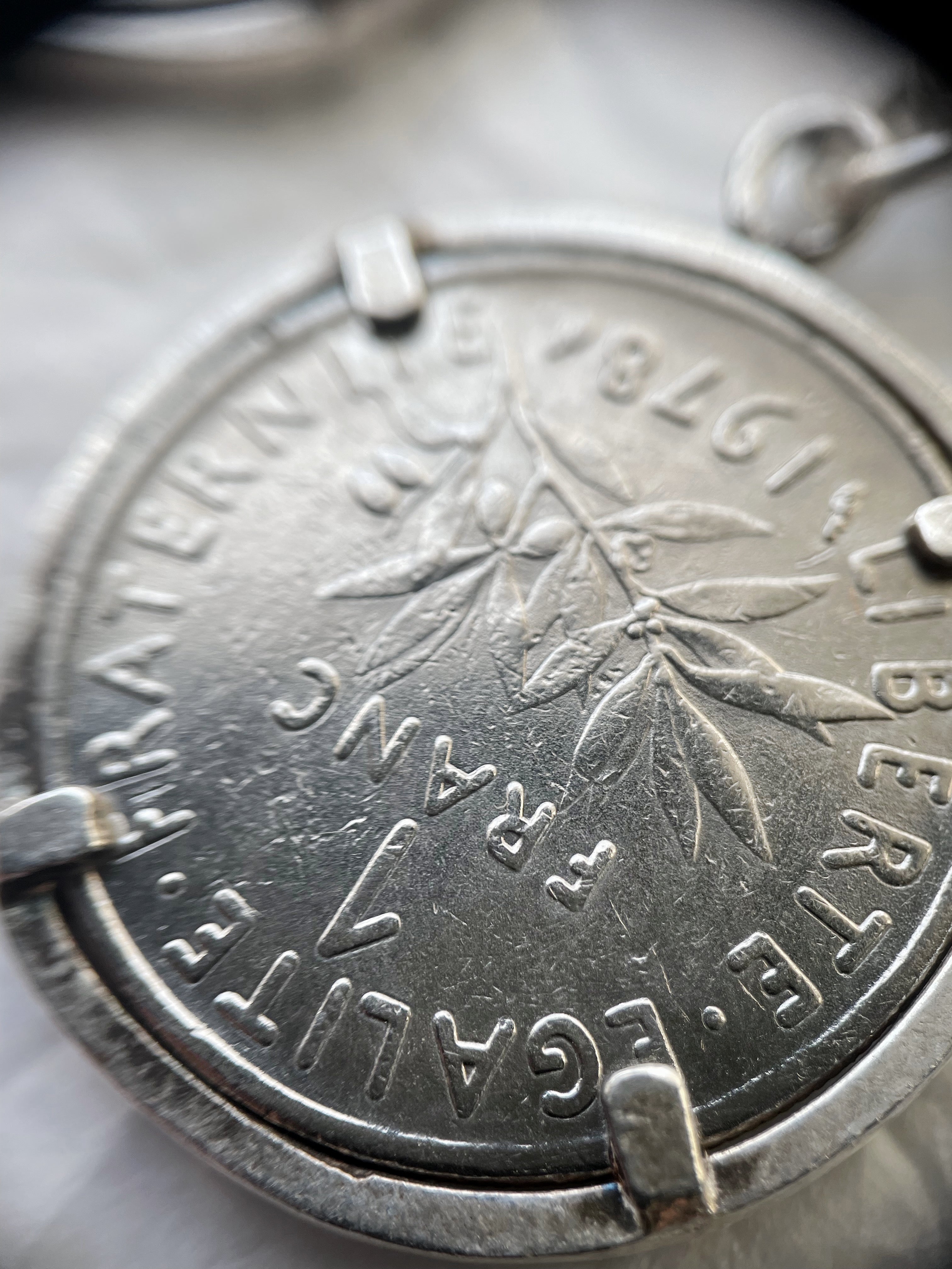 Close-up of Arthus Bertrand sterling silver 1 Franc coin sautoir through jeweller’s loupe showing Franc coin detail – Auric Vintage