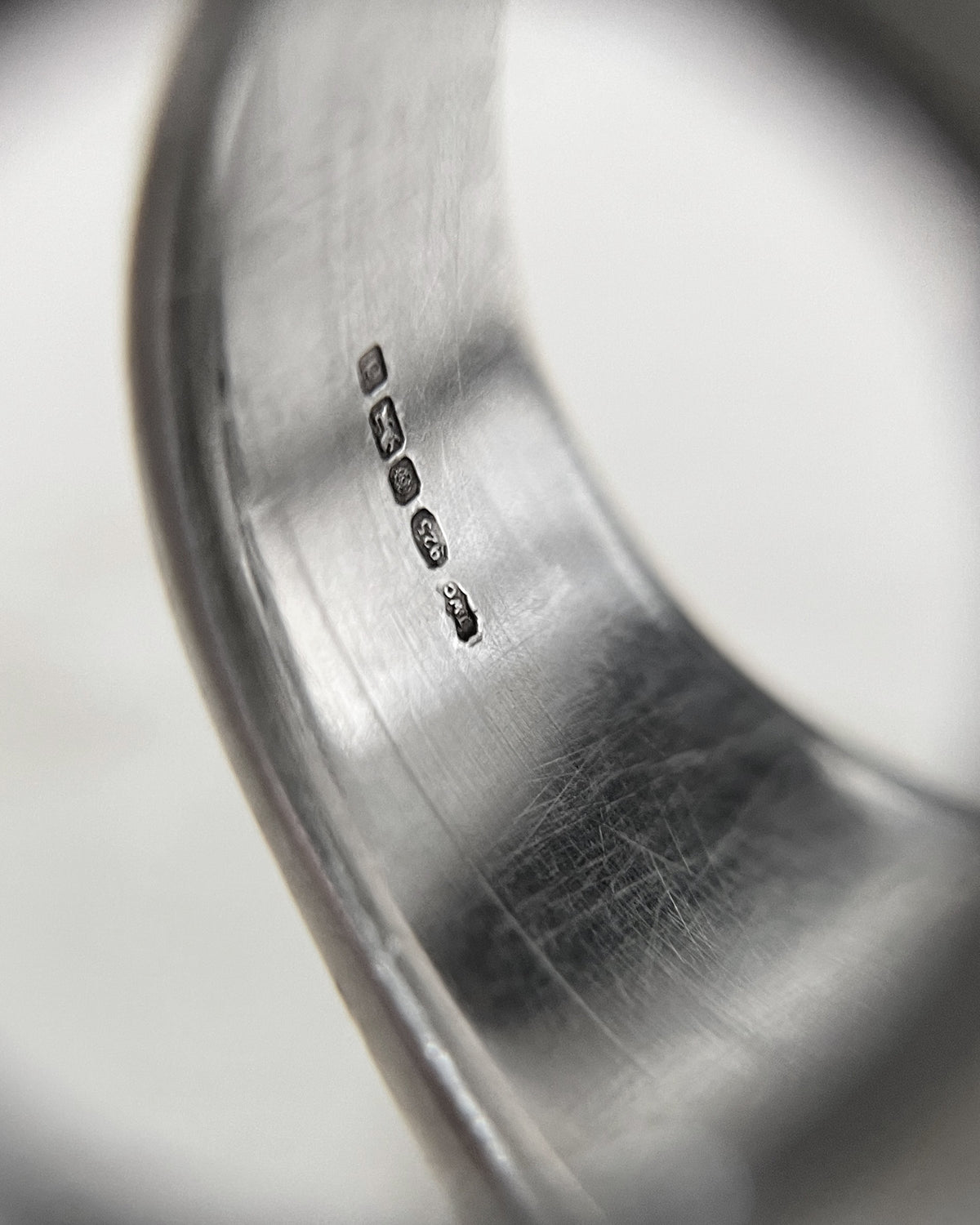 Close-up of the 925 Sterling silver, lion passant and Sheffield 2003 hallmarks inside the shank of a vintage statement ring, viewed through a jeweller's loupe.