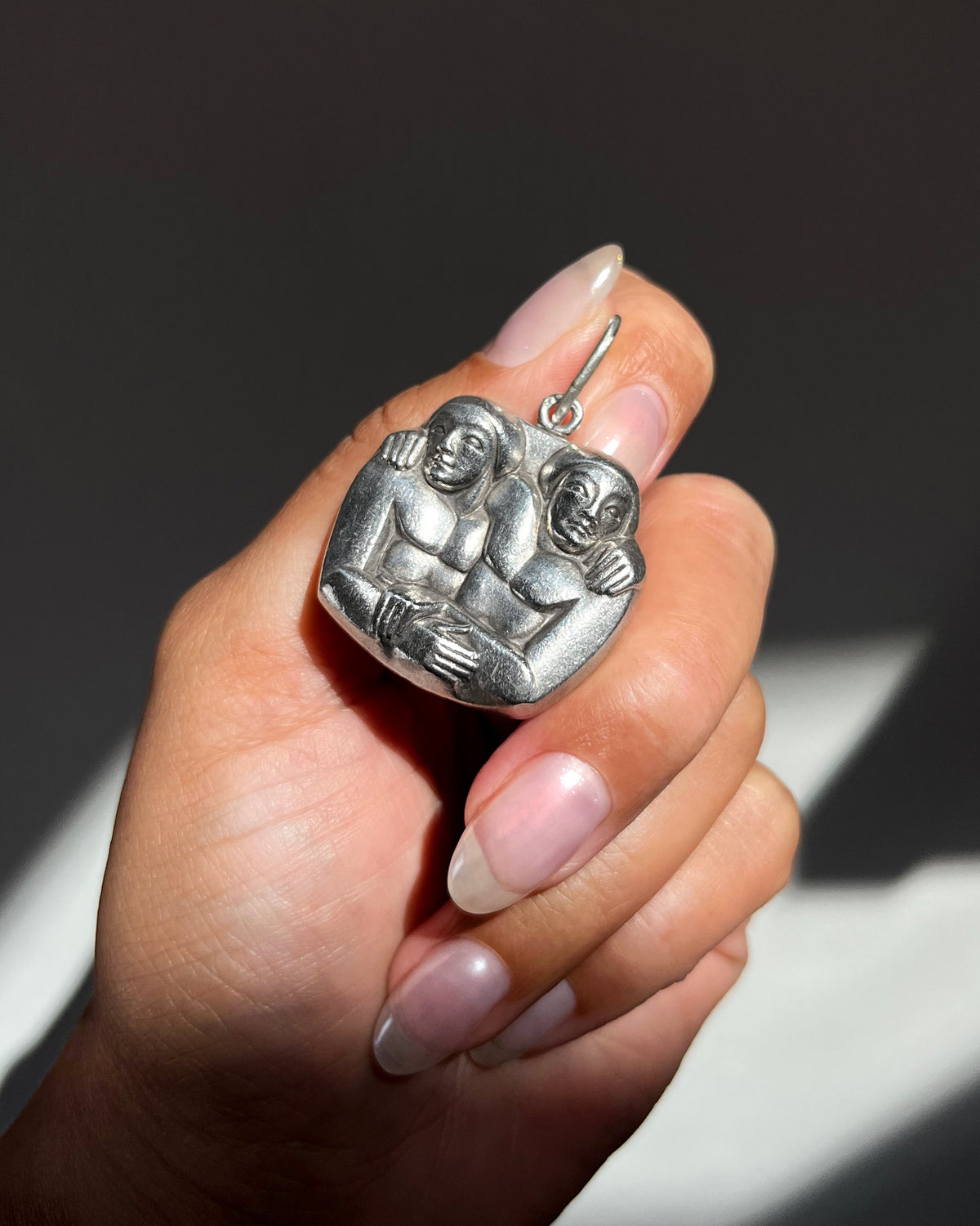 1940s French vintage sterling silver Gemini pendant depicting two carved entwined figures, held in hand for scale