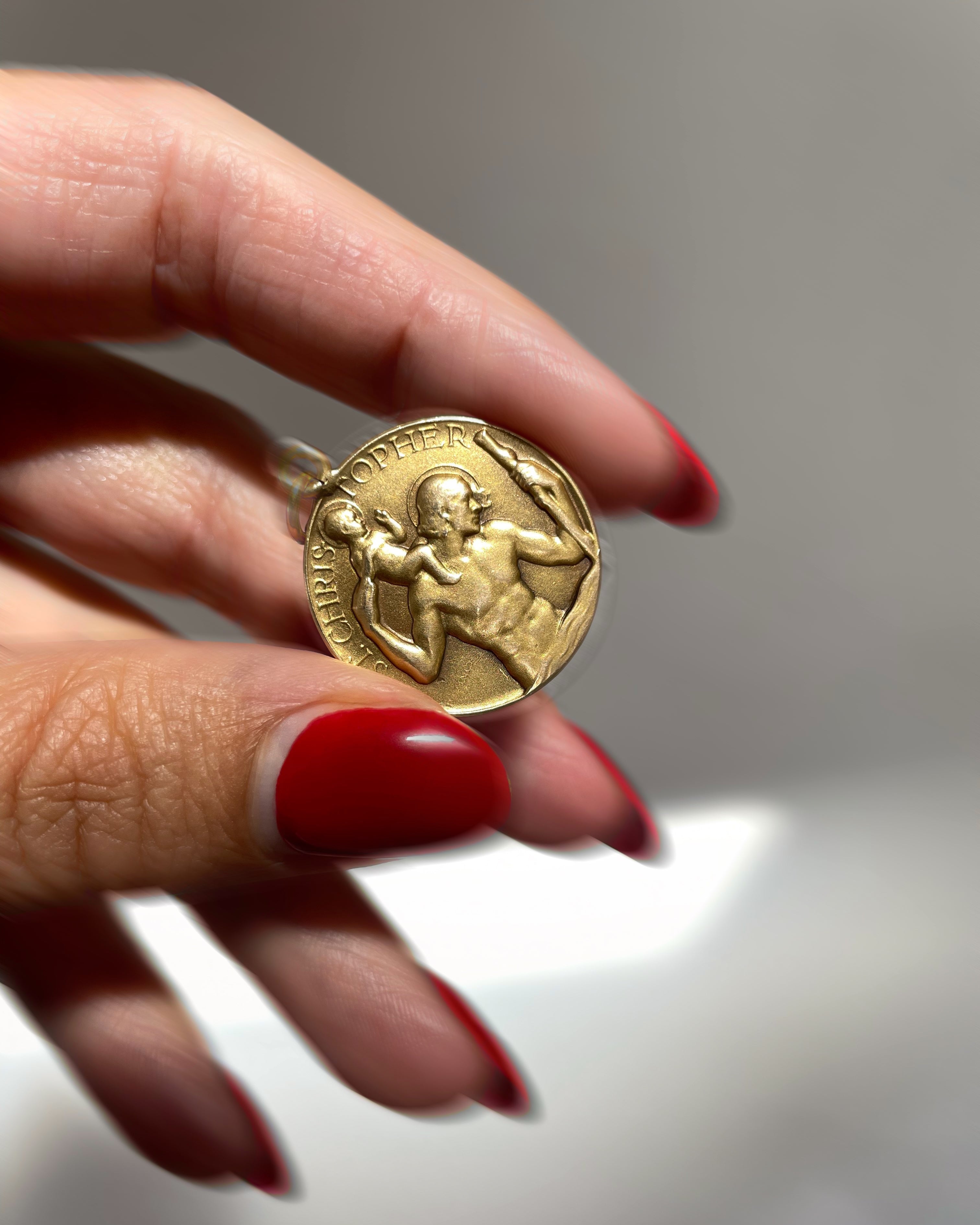 Vintage Paul Vincze 9kt gold St. Christopher medal held in hand for scale – Auric Vintage