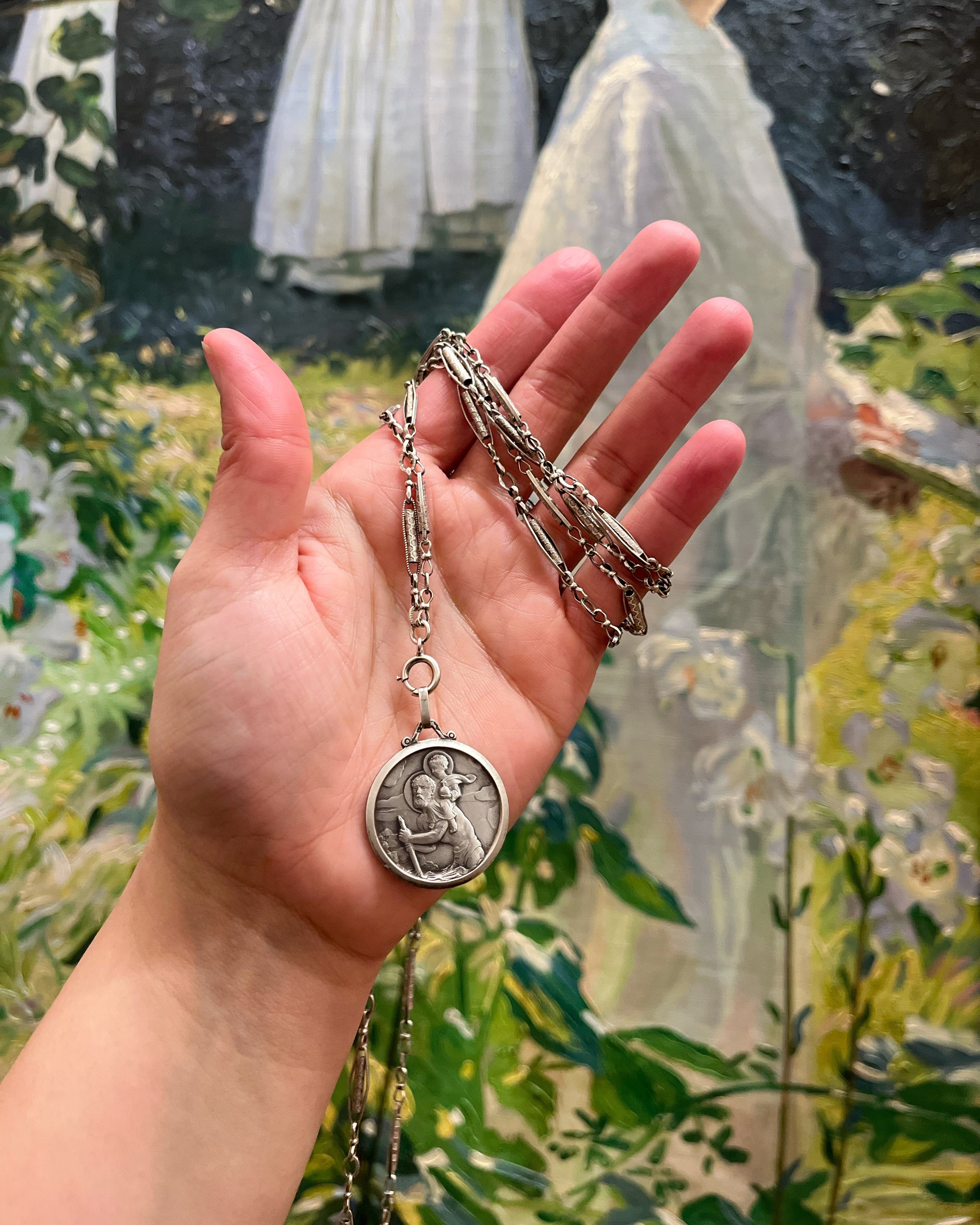 1960s French St. Christopher pendant in silver on chain held in hand showing scale – Auric Vintage