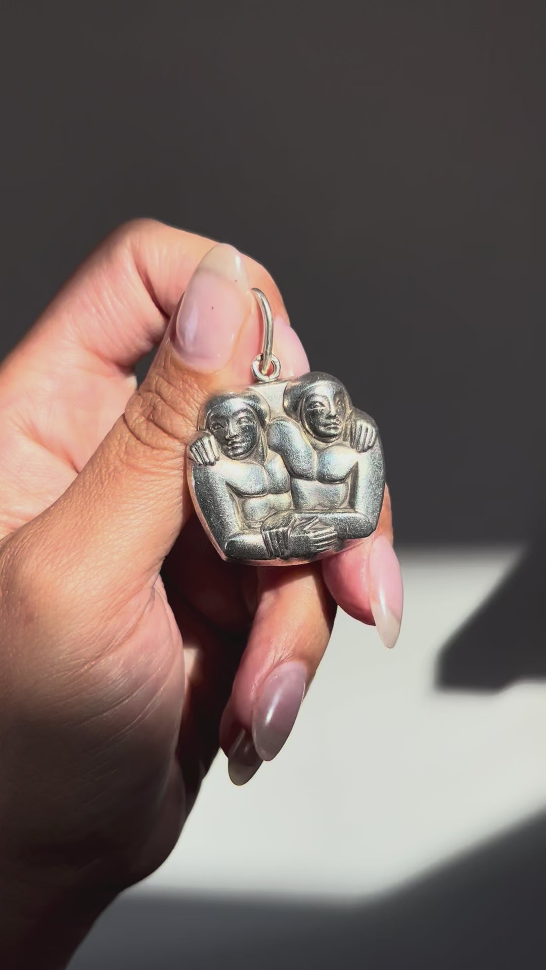 1940s French vintage sterling silver Gemini pendant depicting two angular, entwined figures in a bold Art Deco style, shown held in a hand.