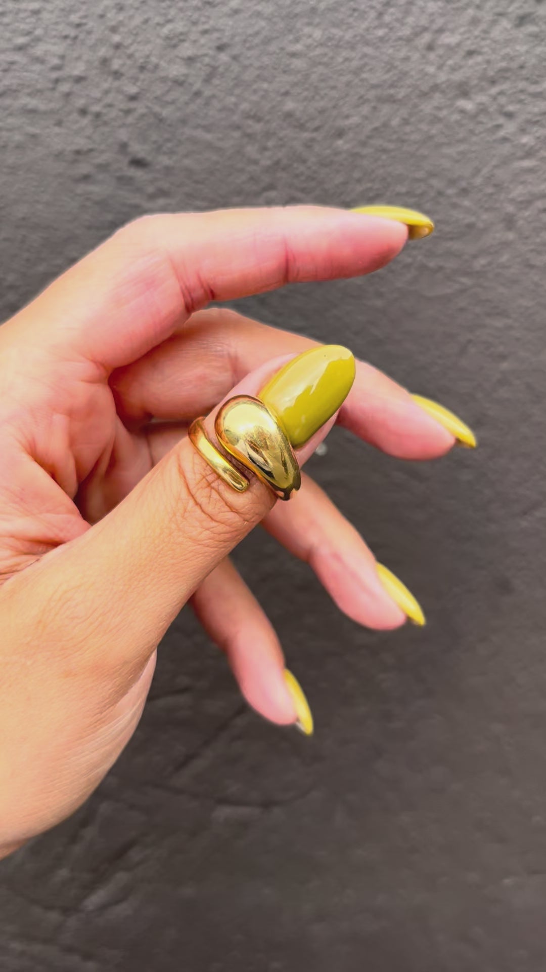 Vintage 18kt gold asymmetric coil ring with a sculptural curved band and polished bulbous end, shown worn on a hand against a grey wall.