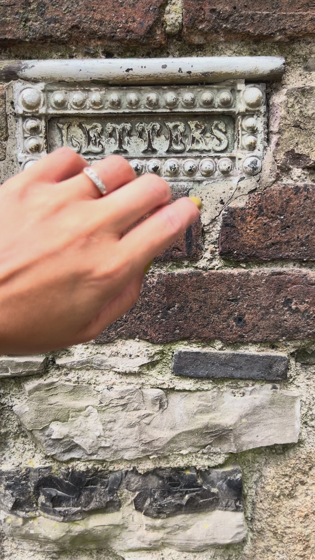 Video of an antique five-stone diamond ring with graduating Old Mine cut diamonds and millegrain platinum settings, shown worn on a hand against a brick wall and letter box.
