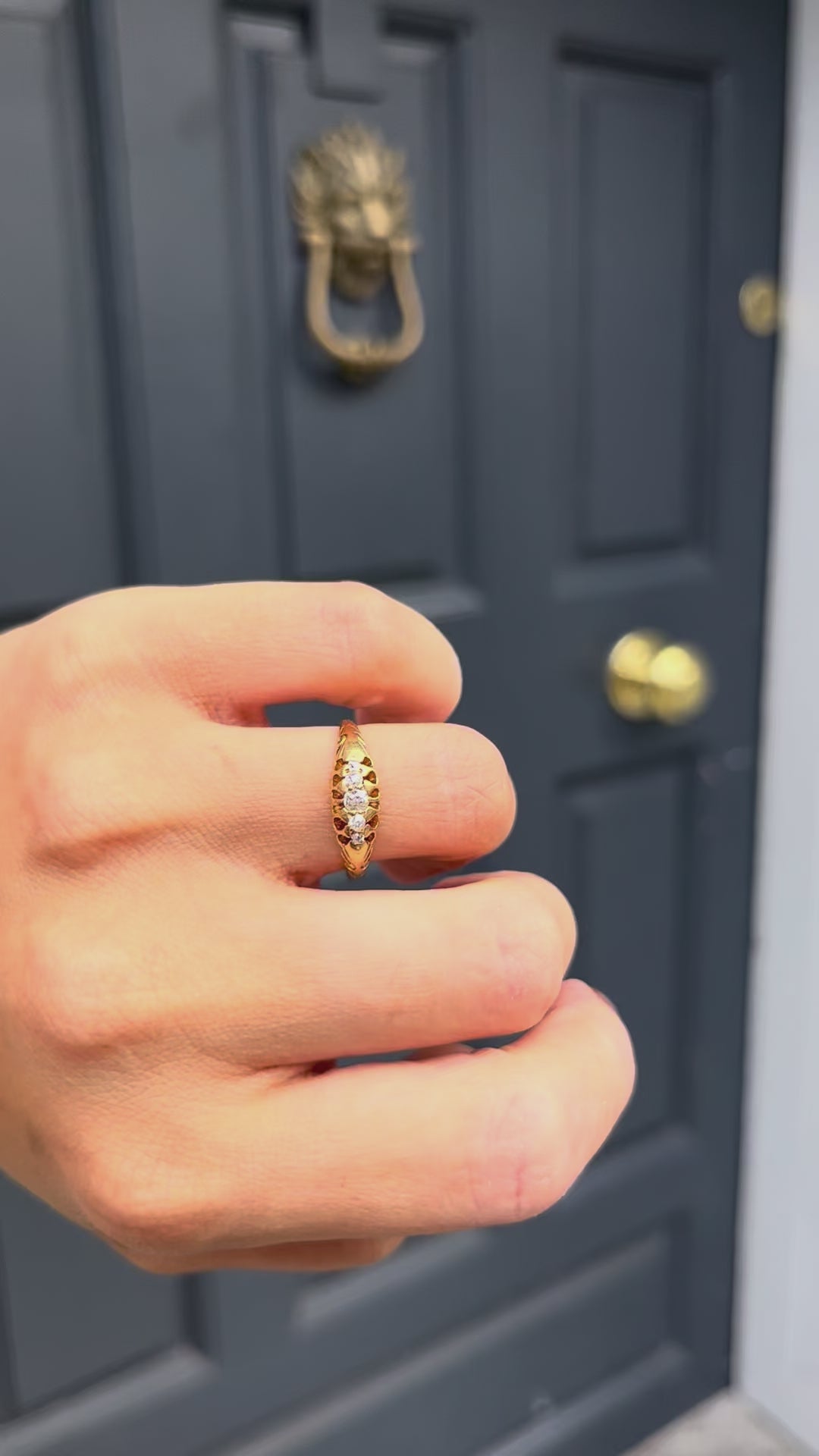 Video of an antique five-stone 18kt gold diamond ring with graduating Old Mine cut diamonds, shown worn on a hand against a blue door.
