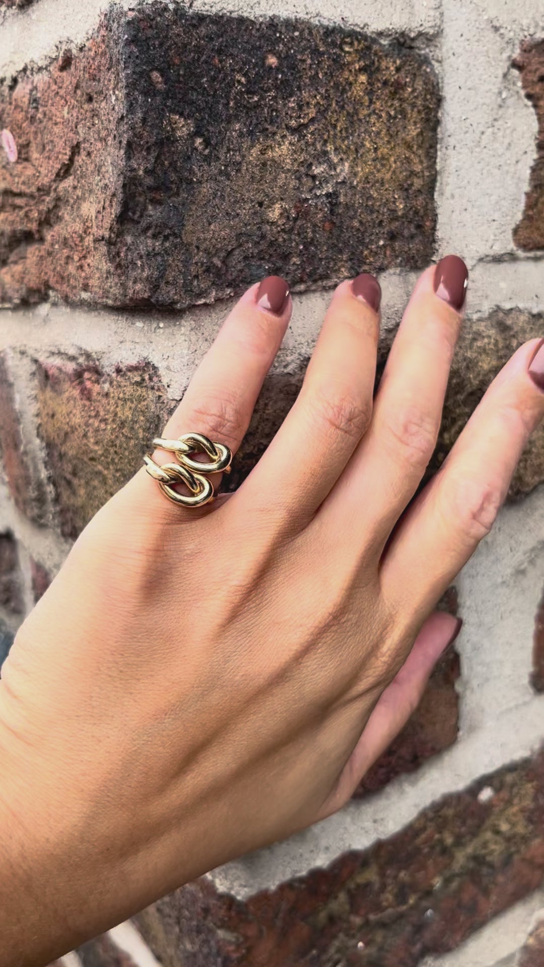 Pair of vintage Irish 9kt gold overhand knot rings stacked together on a pinky finger against a red brick wall.